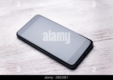 vista dall'alto di uno smartphone con schermo vuoto su un tavolo di legno bianco, tecnologia e concetto di comunicazione, spazio di copia per testo, messa a fuoco selettiva Foto Stock