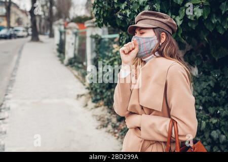 La donna indossa una maschera riutilizzabile all'aperto durante la pandemia del coronavirus covid-19. Ragazza tosse sensazione di malessere. Mantenere la distanza Foto Stock