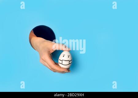 La mano della donna tiene l'uovo attraverso il foro nella tendenza della carta blu, concetto Foto Stock