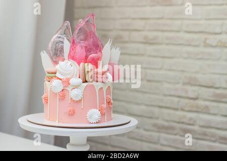 Torta rosa moderna con decorazioni al cioccolato, caramello, macaron francesi, meringhe e carta per waffle. Foto Stock