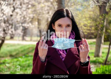 COVID-19. Giovane donna mette su maschera viso medico sterile protettiva all'aperto. Concetto di coronavirus. Foto Stock