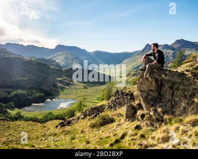 Un camminatore si riposa guardando Blea Tarn, un piccolo lago nel Distretto dei Laghi, Cumbria, Inghilterra. Foto Stock