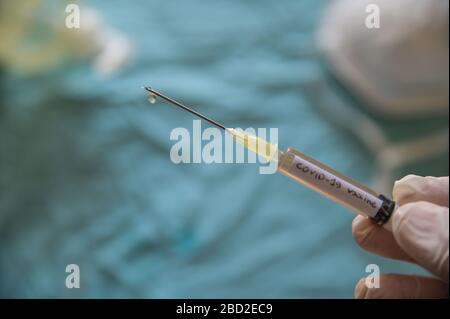 Primo piano di una siringa con la parola vaccino contro il coronavirus. La mano che la tiene preme lo stantuffo e una goccia fuoriesce dall'ago. In Th Foto Stock