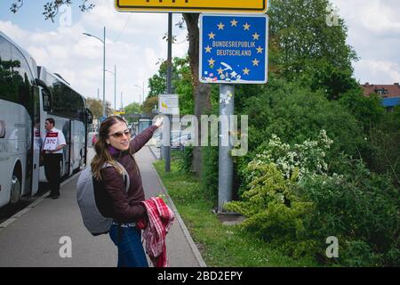 Una giovane donna sta attraversando un confine tedesco, indicando il cartello stradale. Foto Stock