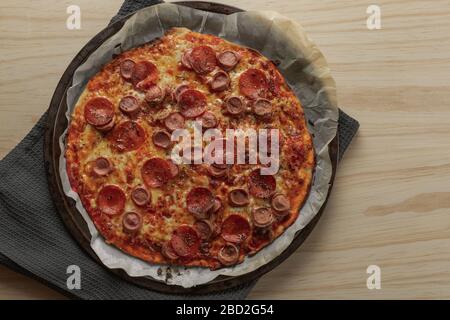 Foto overhead di una pizza fatta in casa con peperoni e salsiccia su vassoio di metallo con un tovagliolo nero in un tavolo di legno Foto Stock