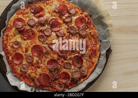 Foto overhead di una pizza fatta in casa con peperoni e salsiccia su vassoio di metallo con un tovagliolo nero in un tavolo di legno Foto Stock