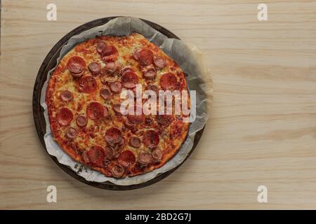 Foto overhead di una pizza fatta in casa con peperoni e salsiccia su vassoio di metallo con un tovagliolo nero in un tavolo di legno Foto Stock