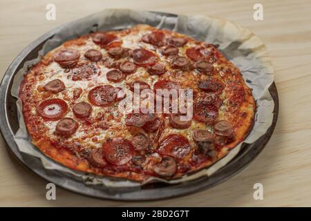 Foto overhead di una pizza fatta in casa con peperoni e salsiccia su vassoio di metallo con un tovagliolo nero in un tavolo di legno Foto Stock