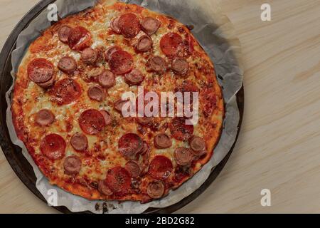 Foto overhead di una pizza fatta in casa con peperoni e salsiccia su vassoio di metallo con un tovagliolo nero in un tavolo di legno Foto Stock