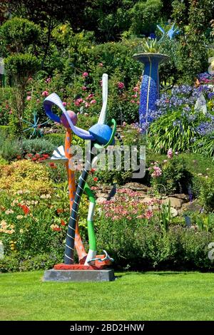 Scena del giardino; scultura whimsical; fiori; erba; arbusti, colorato; urna alto mosaico, la Casa dei Giganti; Akaroa; Nuova Zelanda; estate; verticale Foto Stock