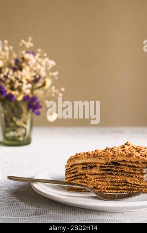 Primo piano dolce casa stratificata torta di miele con prugne essiccate al sole su un piatto bianco con una forchetta d'argento, caffè colazione al caffè Foto Stock
