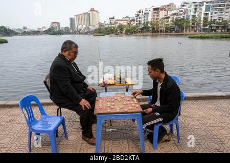 Due uomini giocano Scacchi cinesi da un lago in Hanoi Vietnam. Foto Stock