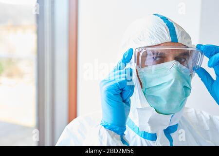 Medico in clinica con indumenti protettivi e occhiali e maschera facciale per l'epidemia di coronavirus Foto Stock