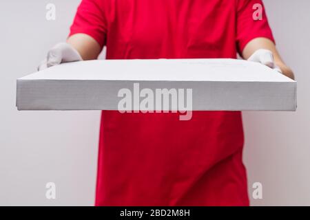 Uomo dal servizio di consegna in t-shirt rossa e guanti di protezione che danno la cassetta della pizza primo piano Foto Stock