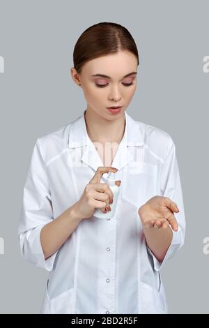 medico donna in uniforme bianca con dispenser di igienizzante su sfondo grigio. stare al sicuro Foto Stock