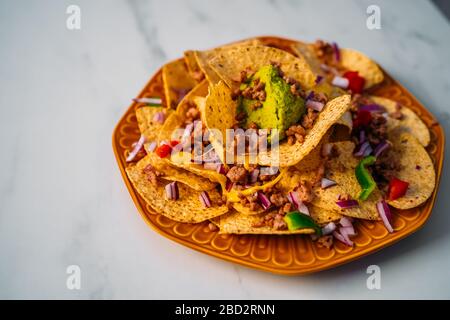 Primo piano di un piatto di deliziose patatine di mais tortilla nachos con salsa di formaggio fuso, manzo macinato, peperoni jalapeno, cipolla rossa, salsa e panna acida Foto Stock