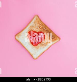 Pane tostato con confettura di fragole a forma di cuore su sfondo rosa Foto Stock