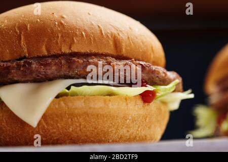 Close-up di freschi e deliziosi fatti in casa burger con lattuga, formaggio, cipolla e pomodoro su un rustico di asse di legno su uno sfondo scuro. Foto Stock