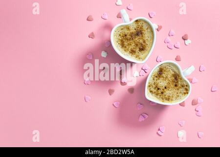 Due tazze da caffè a forma di cuore su sfondo rosa pastello, vista dall'alto con spazio per le copie. Concetto di amore. Foto Stock