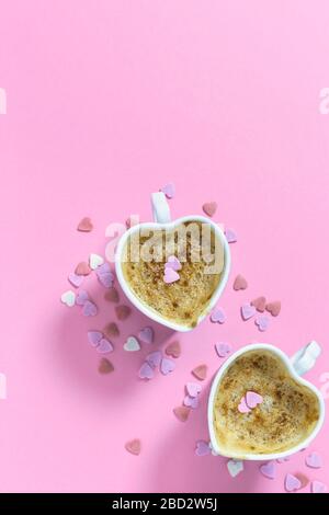 Due tazze da caffè a forma di cuore su sfondo rosa pastello, vista dall'alto con spazio per le copie. Concetto di amore. Foto Stock