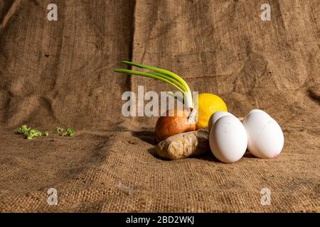 4 uova, cipolla verde, zenzero e limone sul lato destro e broccoli sul lato sinistro, sackcloth sullo sfondo Foto Stock