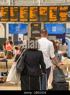 LONDRA, INGHILTERRA - LUGLIO 2018: I viaggiatori ferroviari sull'atrio della stazione di Paddington di Londra che controllano l'imbarco delle partenze elettroniche Foto Stock