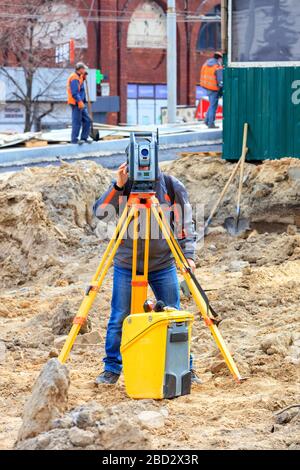 Il tecnico della strada utilizza la livella laser per determinare l'angolo di inclinazione richiesto del tratto stradale in costruzione. Foto Stock