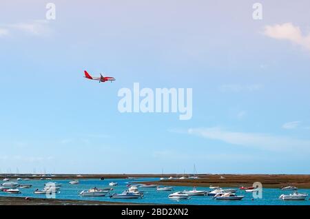 L'aereo vola verso l'aeroporto sul fiume nella città di Faro in Portogallo. Molte barche in una giornata di sole sul fiume. Foto Stock