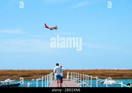 Alto uomo e sua moglie stanno guardando un aereo che vola per l'aeroporto, cielo limpido e una giornata limpida in Portogallo. Barche vela sul fiume nella città o Foto Stock