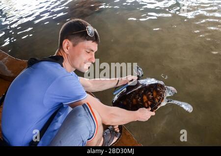 Giovane bruna con fotocamera rilascia tartaruga in acqua, volontario salva tartarughe, protezione degli animali, ragazzo prende le foto di tartaruga. Salvando animali S. Foto Stock