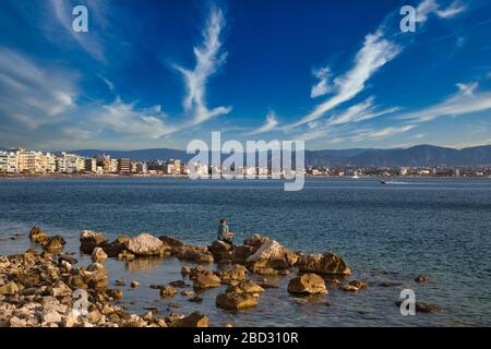 Un pescatore seduto su pietre sulla riva del Golfo di Corinto, Grecia Foto Stock