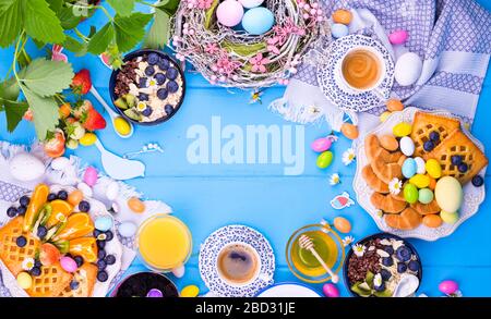 Pasqua colazione appartamento laici. Caffè aromatico fresco, farinata d'avena con frutti di bosco, biscotti, uova colorate e vari dolci pasquali. Vista dall'alto. Spazio di copia. Banner. Foto Stock