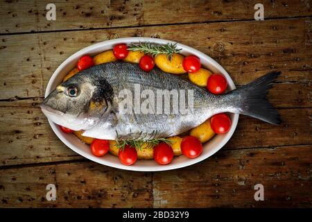 Orata di mare su piatto con patate e pomodori Foto Stock