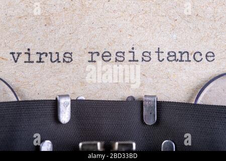 La parola 'resistenza del virus' scritta in caratteri di macchina da scrivere. L'iscrizione nel vecchio stile su carta grigia. Sfondo grigio. Foto Stock