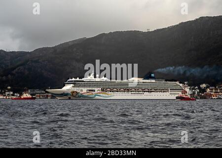 Nave da crociera Norwegian Spirit con partenza dalla banchina di Bontelabo, nel porto di Bergen, Norvegia. Un giorno grigio e piovoso. Due rimorchiatori stanno assistendo, il lavoratore BB e. Foto Stock