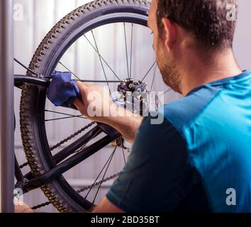 Il meccanico in un negozio di riparazione di biciclette oliatura della catena di una bicicletta. L'uomo mantenendo la sua bicicletta per la nuova stagione di guida. Il processo di lavorazione. Foto Stock