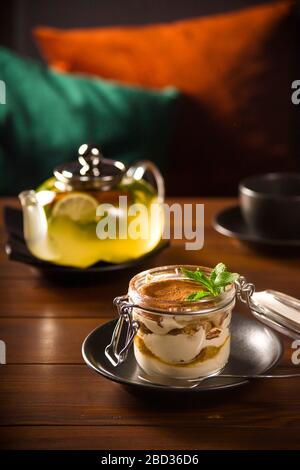 Tiramisù con cacao e menta in un vaso accanto ad un bollitore su un tavolo scuro in un bar. Foto Stock