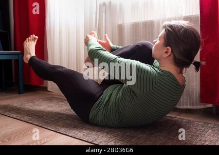 Donna sportiva che si sdraiava e fa esercizio di stretching in soggiorno a casa Foto Stock