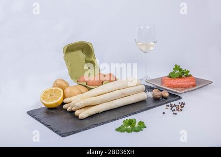 Deliziosi asparagi bianchi di stagione con salsa cremosa di Hollandaise, patate bollite e salmone affumicato a fette su un piatto rustico con limone, wi bianco Foto Stock