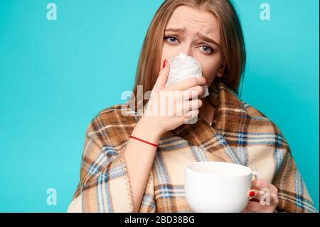 Donna pulisce il naso con un tovagliolo e tiene una tazza di tè caldo nelle sue mani Foto Stock