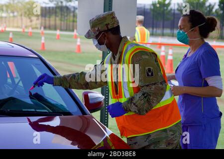 I membri della Guardia Nazionale della Florida assistono i pazienti nei test presso il Drive-Through COVID-19 Mobile Testing Center situato il 4 aprile 2020 a West Palm Beach, Florida. Foto Stock