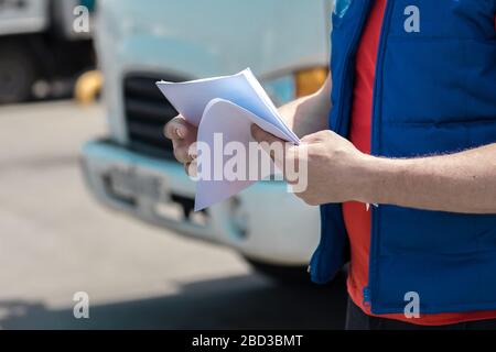 Corriere in uniforme prendendo appunti nel documento e consegna camion bianco lo behinde Foto Stock