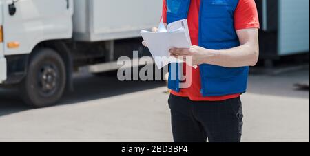 Corriere in uniforme prendendo appunti nel documento e consegna camion bianco lo behinde Foto Stock