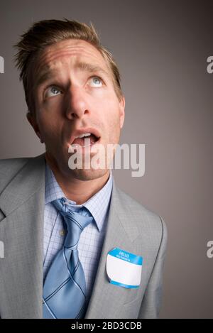 Confuso uomo d'affari che pensa a cosa mettere nel suo vuoto Ciao il mio nome è tag Foto Stock