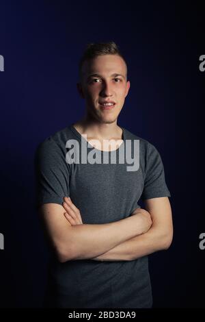 Giovane biondo caucasico in t-shirt grigia su sfondo viola scuro Foto Stock