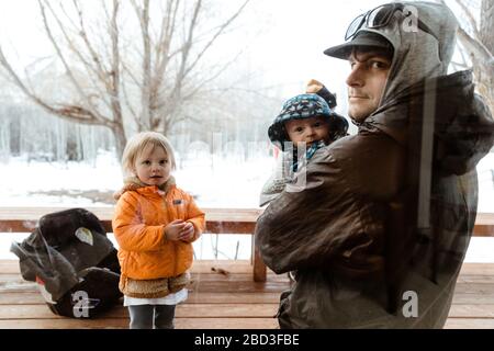 giovane famiglia visita zio in quarantena e guarda attraverso vetro finestra Foto Stock