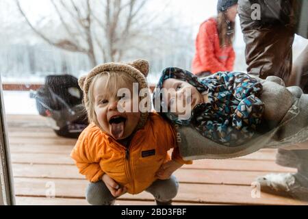 i bambini sorridono e guardano attraverso la finestra lo zio durante la quarantena Foto Stock