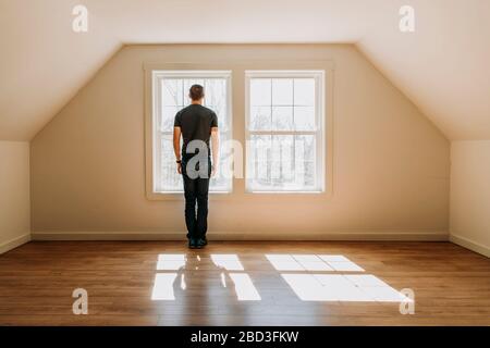 uomo si trova di fronte alla finestra interna in una stanza vuota, solitaria e minimalista Foto Stock