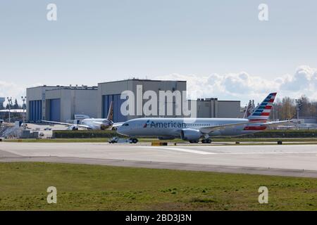 Un Dreamliner 787-8 per American Airlines viene trainato sulla Boeing Flightline presso la Boeing Factory di Everett, Washington, lunedì 6 aprile 2020. Boeing ha prorogato fino a nuovo avviso la sospensione temporanea delle operazioni di produzione in tutti i siti di Puget Sound e Moses Lake. In lontananza si trovano gli appendiabiti della fabbrica Boeing Everett, dove la maggior parte degli aerei a fusolatura larga di Boeing vengono verniciati prima della prova finale di volo. Foto Stock