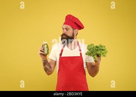 Bere è più facile. Succo di frutta fresco. Frullato di spremitura. Uomo Barbuto chef tenere la lattuga e bottiglia smoothie sfondo giallo. Nutrizione Vegetariana. Frullato di vitamine drink. Frullato Hipster bevanda. Foto Stock